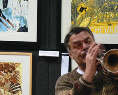 Man in a brown sweater playing trumpet in front of wall with colorful framed animal art.